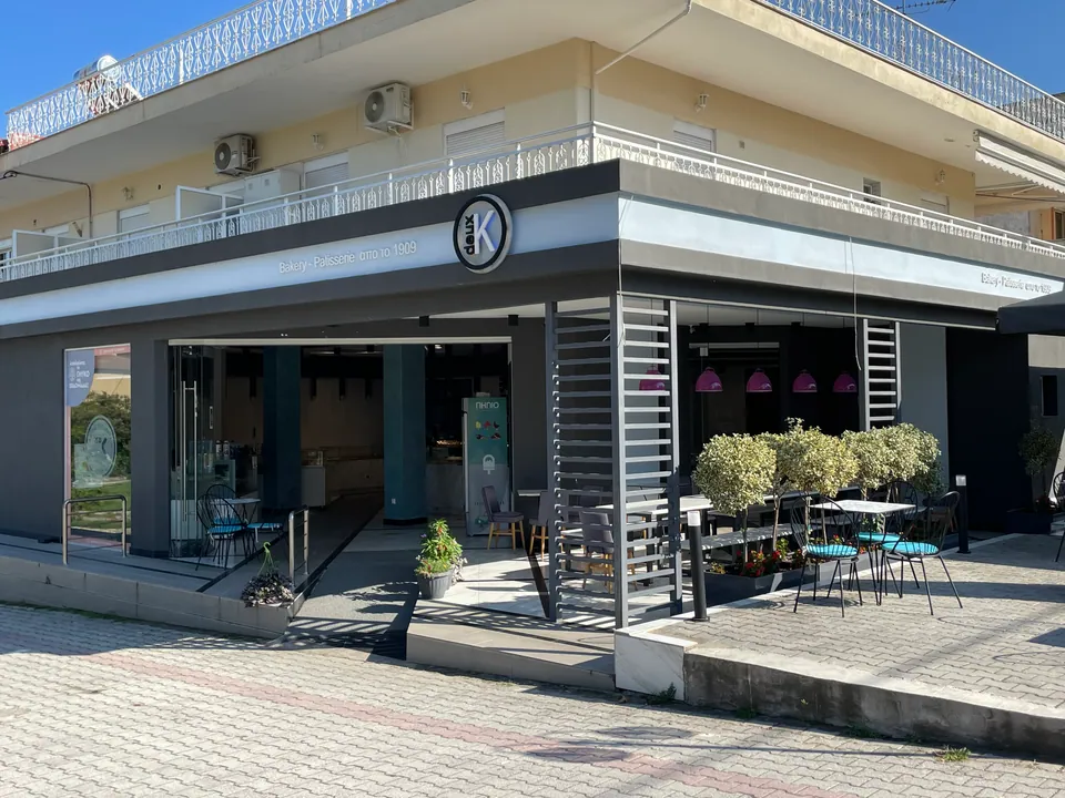Corner view of the ground-floor shop with dark cladding, metal louvres and planted outdoor seating