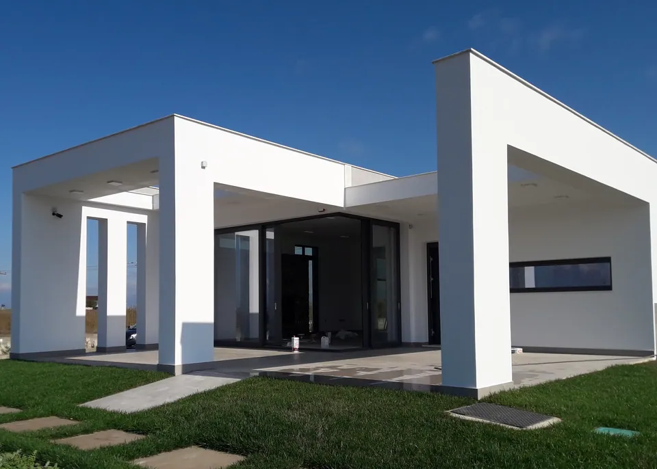 White volumes of the residence with a covered terrace, large glazed openings and stepping stones across the lawn